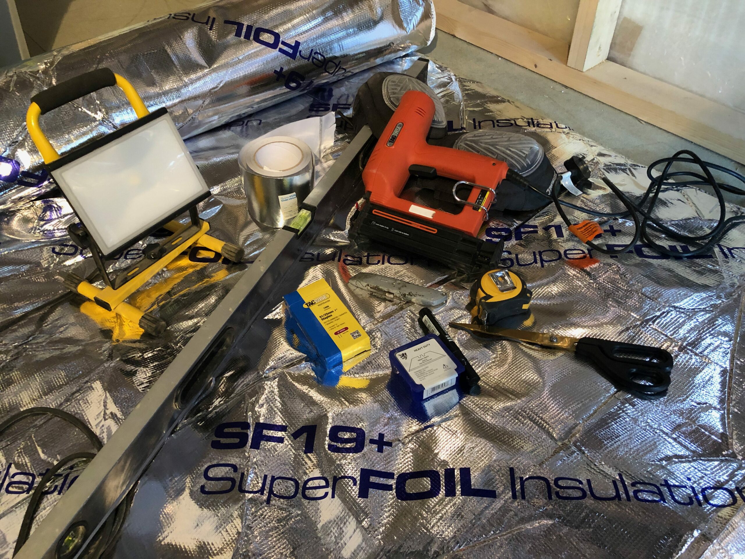 equipment and kit to help install multifoil loft insulation: staplegun, light, spirit level, foil tape, scissors, stanley knife, tape measure, knee pagds