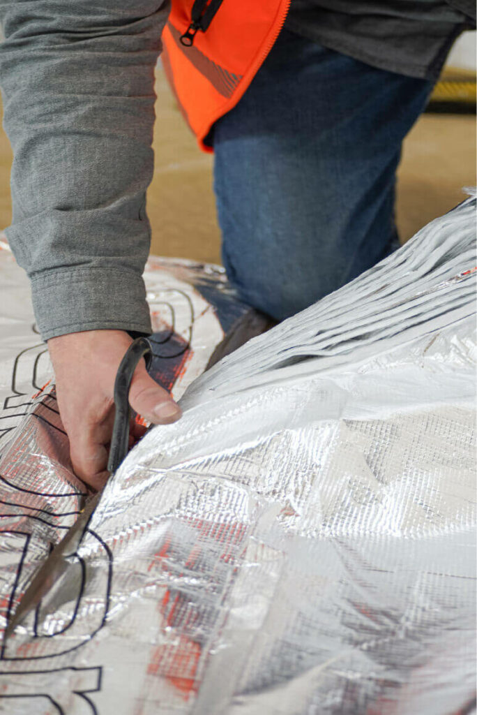 A roll of SuperFOIL being cut using a pair of sturdy shears. The layers of the multifoil are visible along the line of the cut.